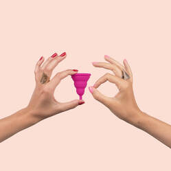 Two hands with different skin tones delicately holding up a silicon menstrual cup