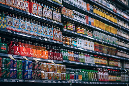 Various types of single-use bottles on a supermarket shelf, including glass, plastic, and aluminum bottles.