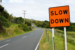 A bright orange sign by the side of a winding road that says 