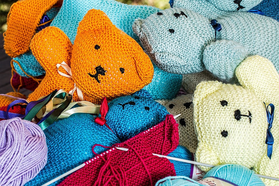 Photo of a bunch of colorful knitted teddy bears in a pile. 