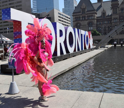 A Toronto Caribbean Carnival performer wearing a hot pink feathered costume as she stands confidently beside the 