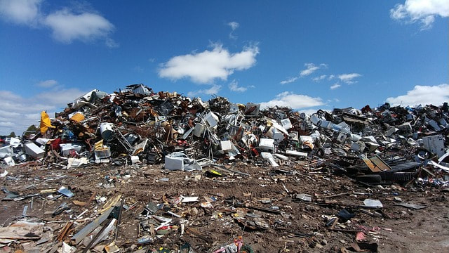 A large landfill full of various plastic and metal items piled upon each other and contrasted against a clear blue sky